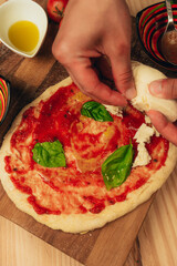 Stock photo of a delicious pizza dough with tomato and basil leaves and a hand putting fresh...