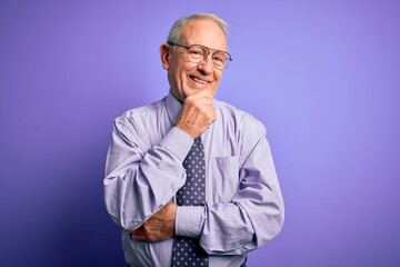 Grey haired senior business man wearing glasses standing over purple isolated background looking confident at the camera with smile with crossed arms and hand raised on chin. Thinking positive.