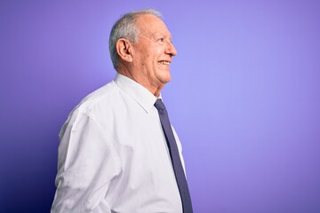 Grey haired senior business elegant man standing over purple isolated background looking to side, relax profile pose with natural face with confident smile.