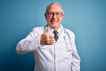 Senior grey haired doctor man wearing stethoscope and medical coat over blue background doing happy...