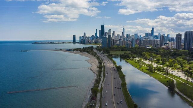 Flying towards Chicago Downtown skyscrapers above highway by the Lake Michigan with fast moving clouds and cars. Aerial Hyperlapse 