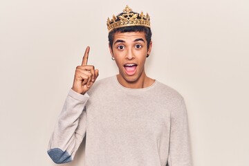 Young african amercian man wearing prince crown pointing finger up with successful idea. exited and...