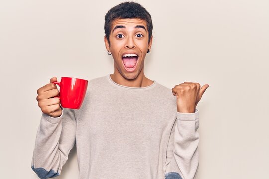 Young african amercian man holding coffee pointing thumb up to the side smiling happy with open mouth