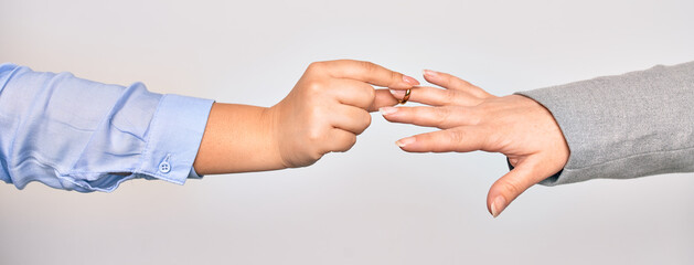 Hand of caucasian young woman putting golden marriage ring to other person over isolated white background
