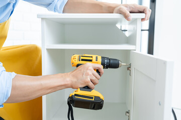 Close up portrait and details of caucasian male worker using electric screwdriver instrument in hand and repairing new wooden desk, home improvement concept.