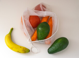 Photo of a bunch of different fruits and vegetables inside a reusable bag. There is a banana, avocados, carrots and tomatoes. Zero Waste concept