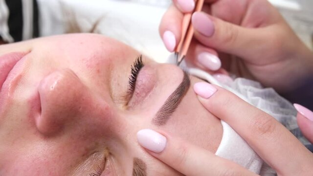 Permanent make-up for eyebrows of woman with thick brows in beauty salon. Closeup beautician doing coloring tattooing eyebrow.