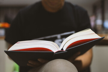 young man is sitting reading in the window in the room with soft-focus and over light in the...