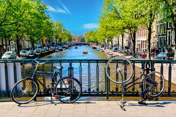 Fototapeta na wymiar Old bicycles on the bridge in Amsterdam, Netherlands against a canal and old buildings during summer sunny day. Amsterdam postcard iconic view. Tourism concept.