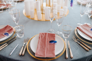 Banquet table with blue velvet tablecloth. Plates and cutlery, butlers smeralda glasses, pink velvet napkins, candles. High stand of roses, hydrangeas.
