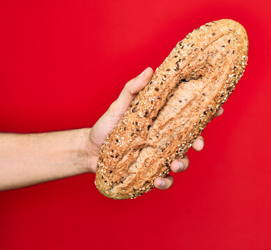 Beautiful hand of man holding wholemeal integral bread with cereals over isolated red background