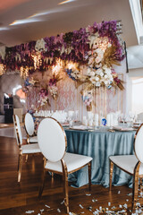 Banquet table with blue velvet tablecloth, candles, Alexa Dining Chair. High stand with a composition of rose flowers, hydrangeas, golden leaves. Against the background of golden racks with flowers, s