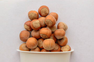 Hazelnuts in shell. A plastic cup. White background. Concept of healthy food, vegetarianism.