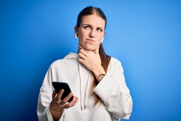 Young redhead sportswoman doing sport listening to music using earphones and smartphone Touching painful neck, sore throat for flu, clod and infection