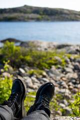 Photo of two black elegant boots sitting on the nature comtemplating a green landscape next to the sea.