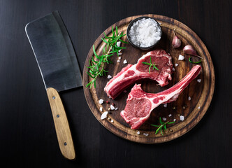 Two raw lamb chops on a wooden cutting board with spices on a dark wooden background © Ekaterina Belova