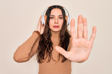 Young beautiful woman with blue eyes listening to music and dancing using headphones with open hand doing stop sign with serious and confident expression, defense gesture