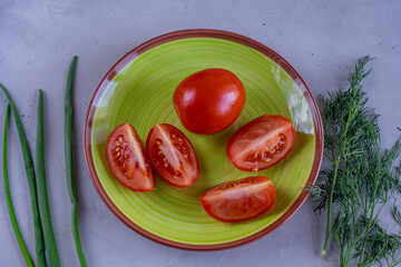 Sliced tomatoes on green plate surrounded by fresh green onion and dill