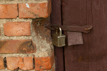 Rusty locked padlock on a wooden dilapidated door of a pauper dwelling or barn shed