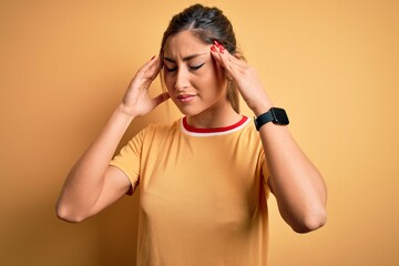 Young beautiful athletic woman wearing casual t-shirt and ponytail over yellow background with hand on head for pain in head because stress. Suffering migraine.