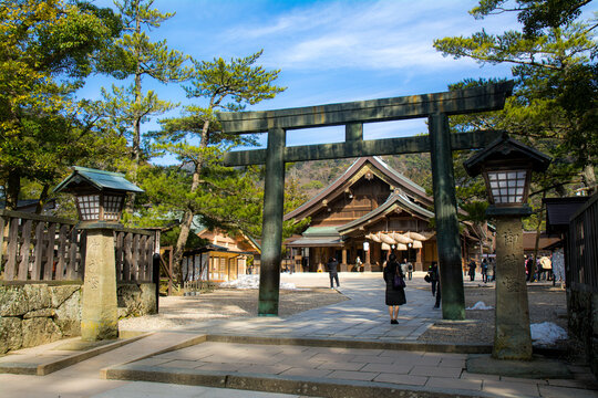 Kane-no-Torii (Bronze Torii) in Izumo Taisha Shrine with two lamps on each side with the kanji characters "The God's Lamp". Behind the torii is the Haiden (Worship Hall) of the shrine.