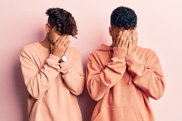 Young gay couple wearing casual clothes with sad expression covering face with hands while crying....