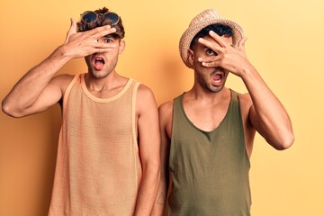 Young gay couple wearing summer clothes peeking in shock covering face and eyes with hand, looking through fingers with embarrassed expression.