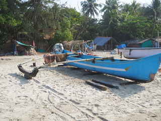 A view of an old battered blue wooden fishing boat standing on a sandy beach.