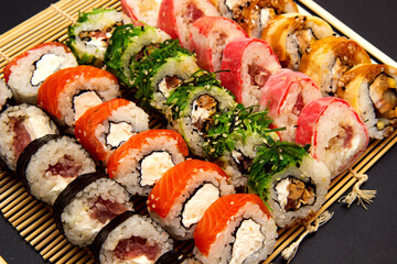 sushi set with different maki - hosomaki, futomaki and uramaki on bamboo mate with chopsticks on a black background.