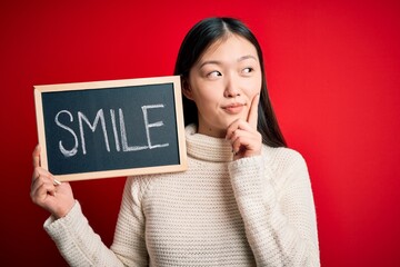 Young asian woman holding blackboard with smile word as hapinness message serious face thinking...