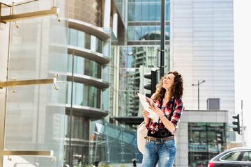 Portrait of young attractive woman looking on map in the middle of the city
