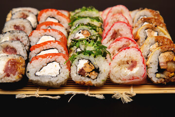 sushi set with different maki - hosomaki, futomaki and uramaki on bamboo mate with chopsticks on a black background.