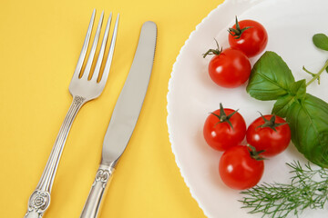 Chery tomatoes on a plate with basil and cutlery.