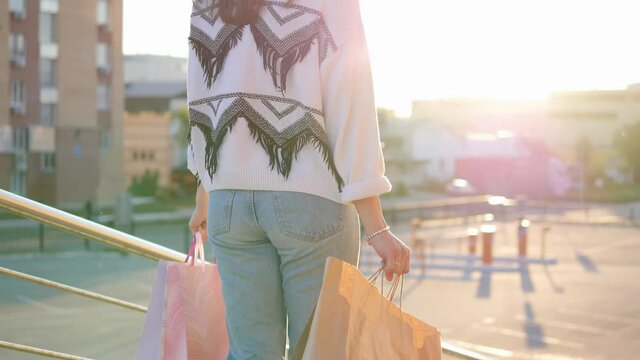 Woman with shopping bags walking in a city at sunset. A girl walks along the road after shopping with full bags. Shopping after quarantine
