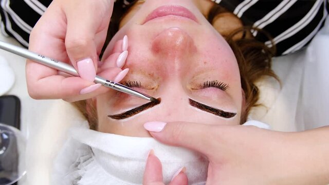 Permanent make-up for eyebrows of woman with thick brows in beauty salon. Closeup beautician doing coloring tattooing eyebrow.
