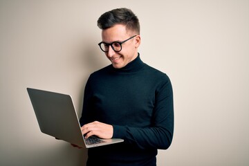 Young handsome caucasian business man wearing glasses using computer laptop with a happy face standing and smiling with a confident smile showing teeth
