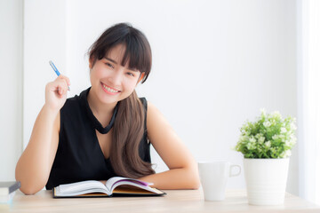 Beautiful young asian woman smiling sitting study and learning writing notebook and diary in the living room at home, girl homework, business woman working on table, education concept.