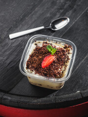 Tiramisu with berries in plastic container on the wooden barrel