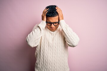 Young handsome latin man wearing white casual sweater and glasses over pink background suffering from headache desperate and stressed because pain and migraine. Hands on head.