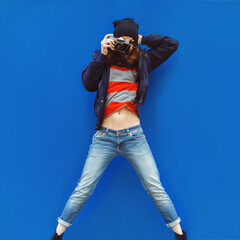 portrait of a beautiful girl with a camera hipster jumping on the background of blue wall outddor