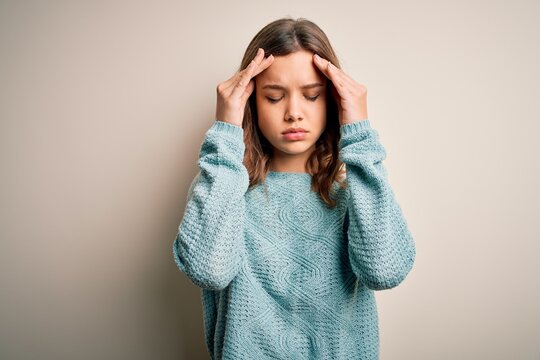 Young blonde girl wearing casual blue winter sweater over isolated background with hand on head for pain in head because stress. Suffering migraine.
