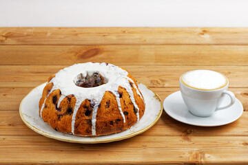 Freshly baked homemade raspberry cake with white sugar icing and cup of coffee latte on wooden table. Shallow focus.