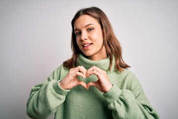 Young beautiful blonde girl wearing winter sweater standing over isolated background smiling in love showing heart symbol and shape with hands. Romantic concept.