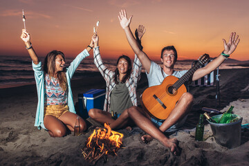 Group of friends relaxing around bonfire on the beach at sunset