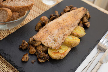 fried trout fillet on pillow of fried champignon mushrooms on dark warm stone plate