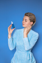 one cute woman with a short haircut looks at a cosmetic product for the face on a blue background . home after shower