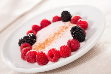raspberries and blackberries laid out on a white plate in circle with yogurt and cinnamon