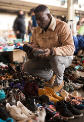Afro-American guy considers sacond hands shoes on flea market