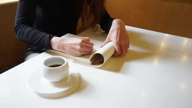 a Hand of a girl draws in sketchbook with a pencil in a cafe, a cup of coffee on the table, short Travelling shot