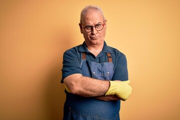 Middle age cleaner man cleaning wearing apron and gloves over isolated yellow background skeptic and nervous, disapproving expression on face with crossed arms. Negative person.